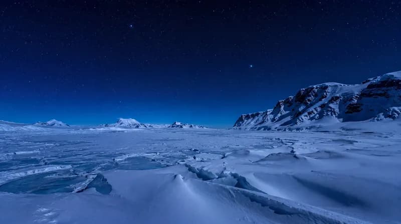 Arctic Night Frozen arctic sea with ice ridges and snow-covered mountains under a starry blue night sky